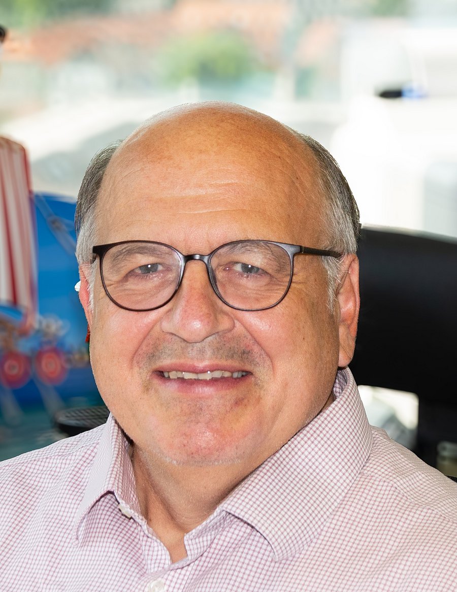 The picture shows an older man with glasses, a bald head on top with some gray hair on the sides, and a friendly smile.