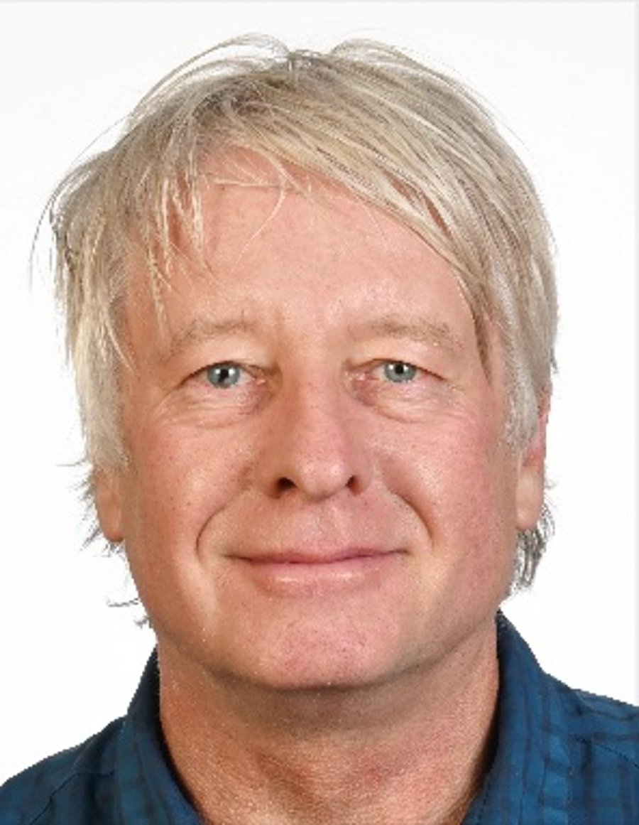 A smiling white man with light gray hair and blue eyes looks head-on into the camera. He is wearing a dark blue shirt.