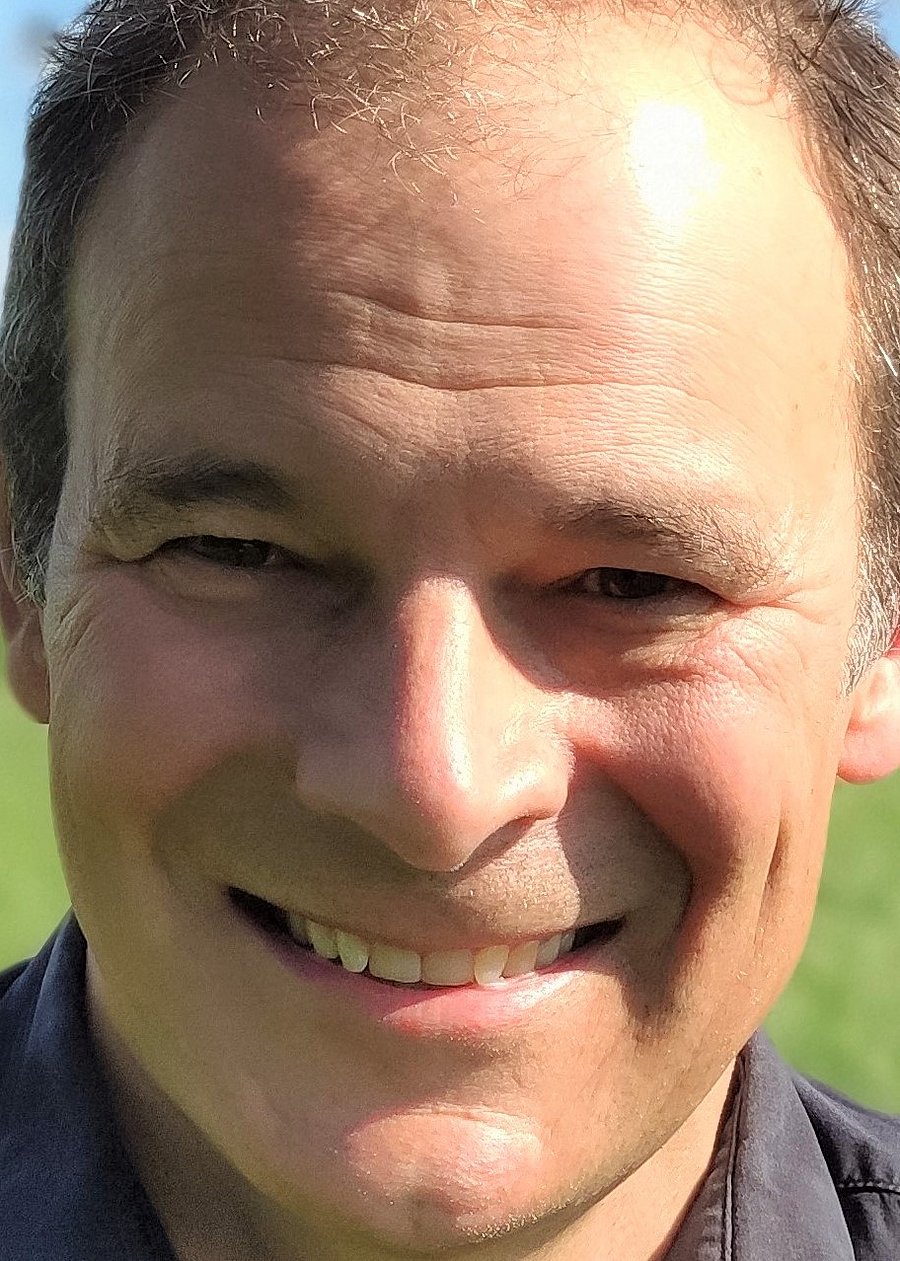 Portrait of Dr. Hans Marten Paulsen which is taken outside in a meadow. It shows a middle-aged, smiling man with brown, greying hair.