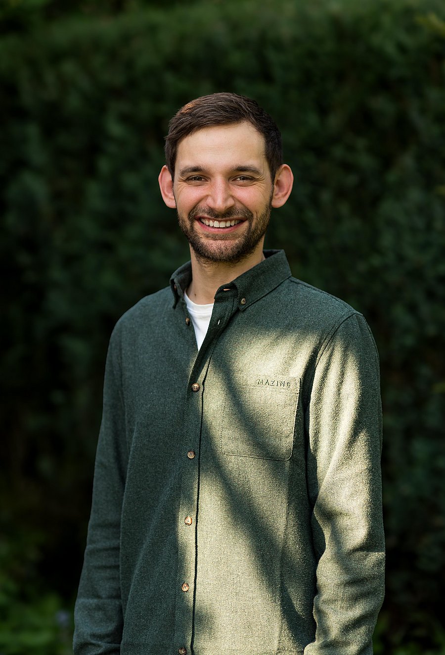 A photo of Große Kleimann. It shows a young smiling man facing the camera. He has dark blond hair, a beard and wears a dark green shirt.