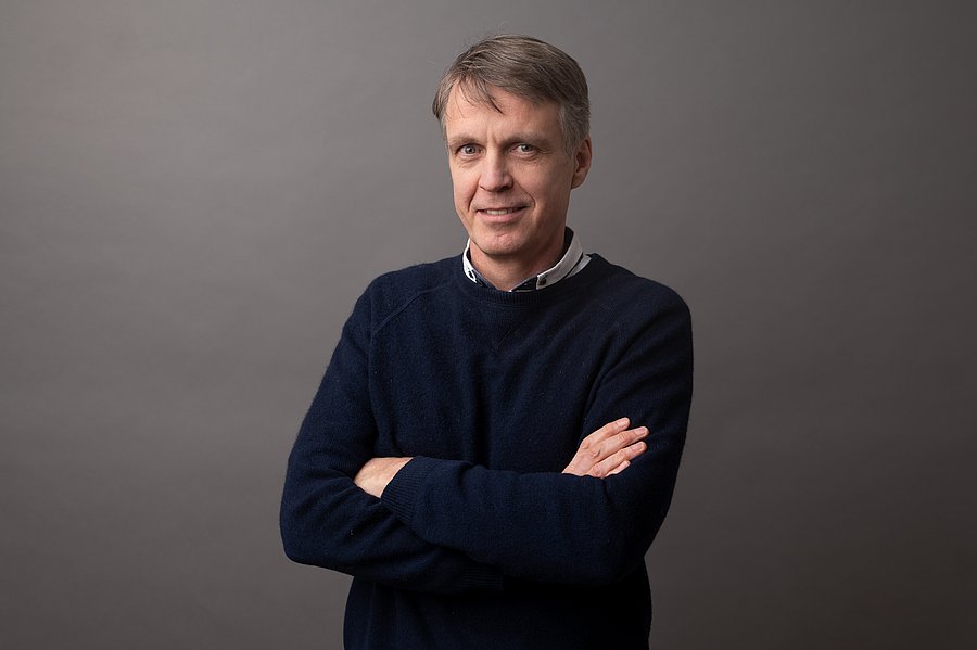 A photo of Dr. Rolf Sommer. He is middle-aged with dark blond hair and blue eyes. He is wearing a shirt with a dark blue sweater, arms crossed, against a gray background.