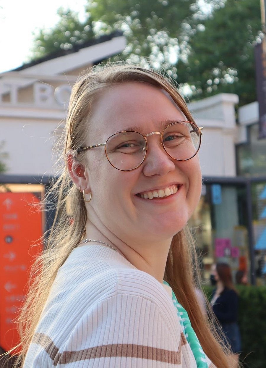 A photo of Laura Harbo. It shows a young woman with glasses and long, blonde hair, and a white and brown shirt