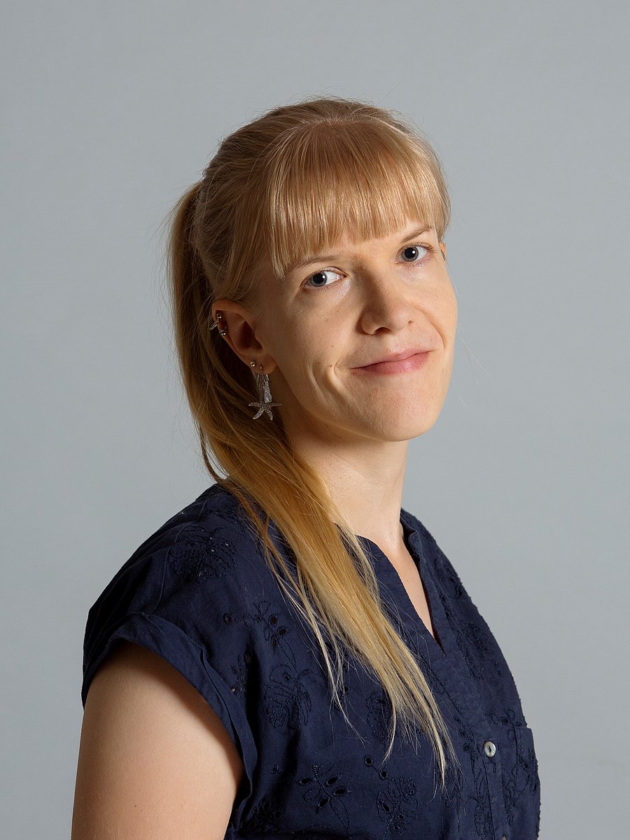 A photo of Elisa Vainio. It shows a smiling woman with blonde hair wearing a dark blue sleeveless shirt. 