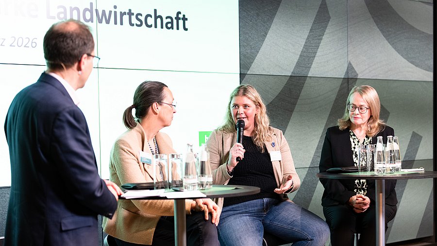 Eine vierköpfige Gruppe von Referentinnen und Referenten diskutiert engagiert auf einer Bühne anlässlich der Fachkonferenz „Starke Frauen – starke Landwirtschaft“ des Bundesministeriums für Landwirtschaft, Ernährung und Heimat.