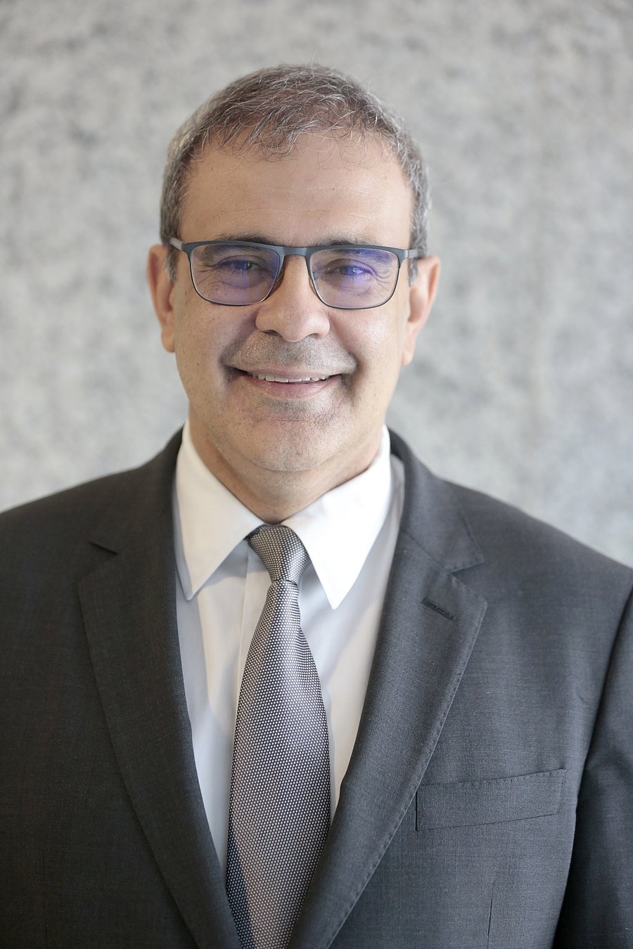 A photo of Eduardo Sampaio Marques. It shows a smiling man looking directly into the camera. He has grey hair, wears glasses and a grey suit over a white shirt with tie.