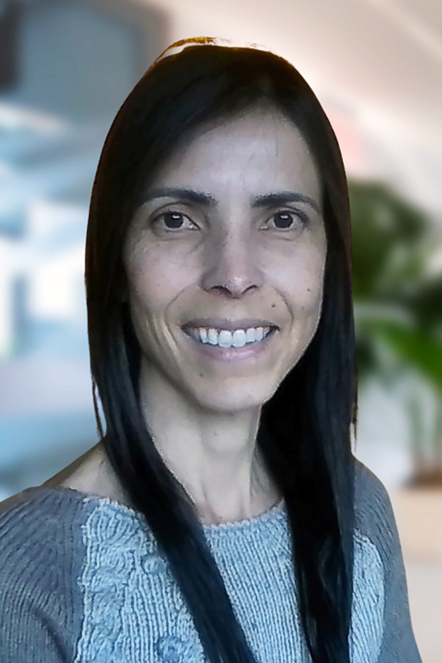 Portrait of Dr Carolina Lisboa, Manager for Agriculture Innovation at Verra. It shows a smiling woman with dark hair looking straight into the camera. She wears a grey and white sweater.